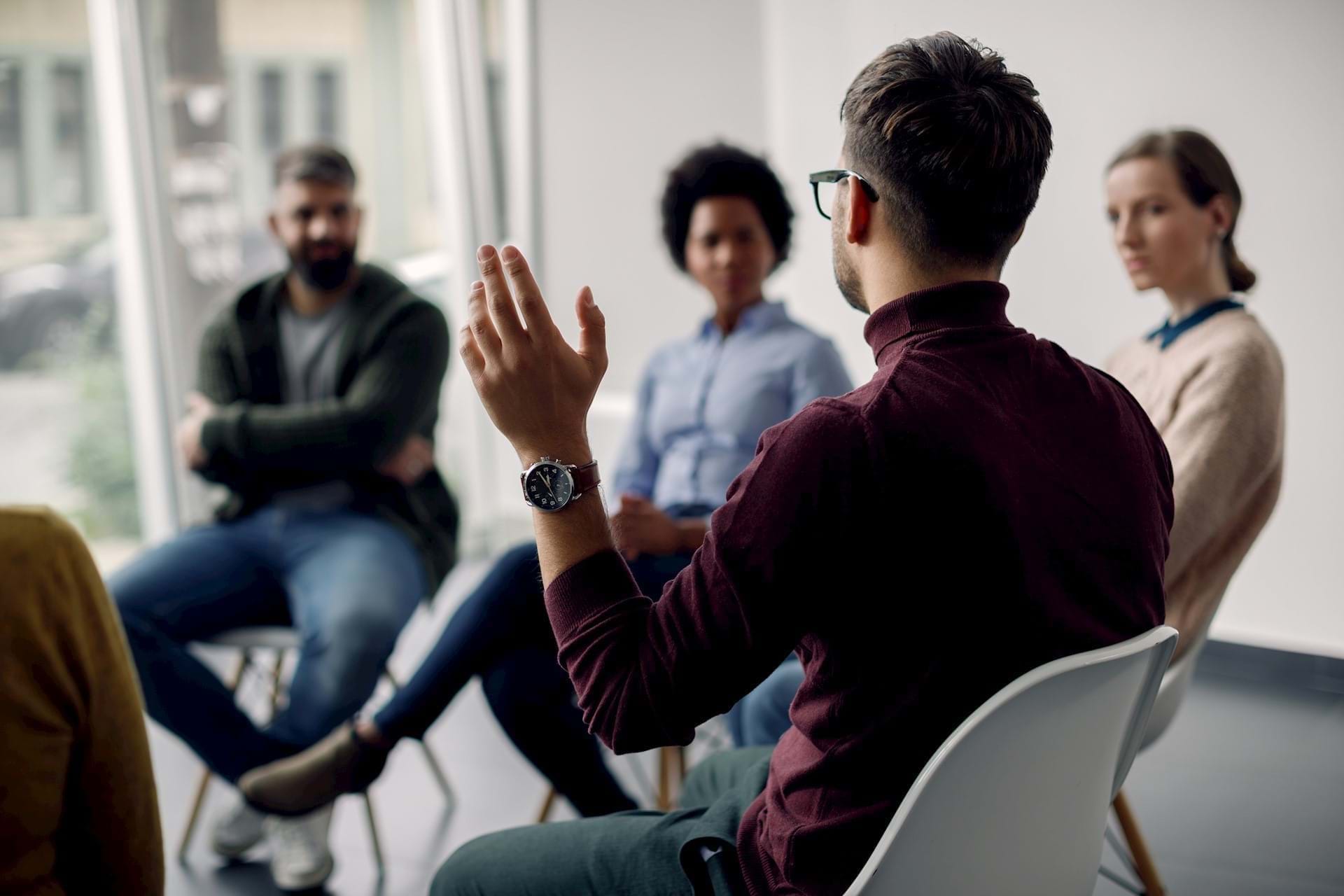 Blurred image of colleagues in an informal meeting setting - one colleague is facing away from camera and is holding up his hand