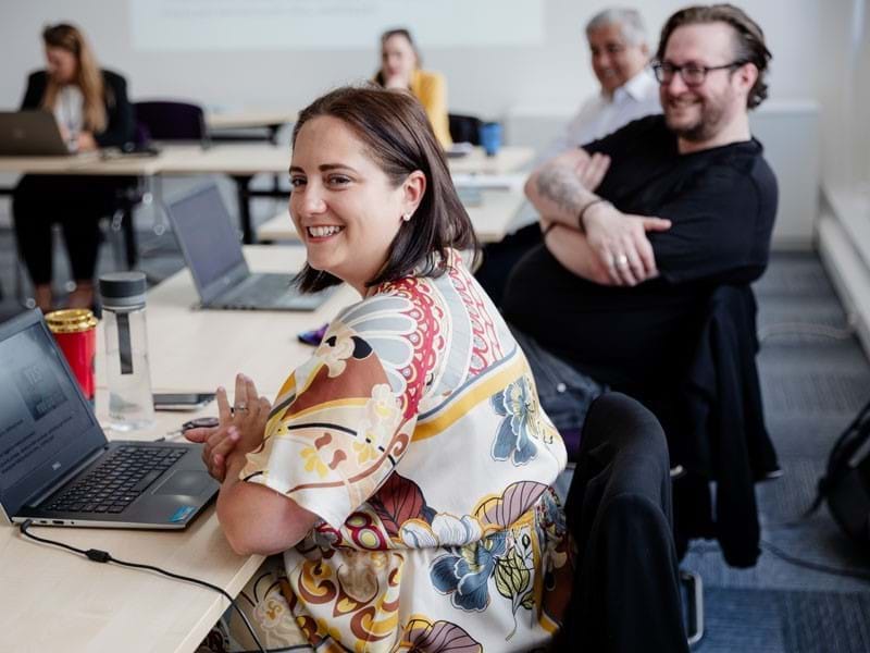 Image of colleagues smiling in a meeting with laptops on their desks