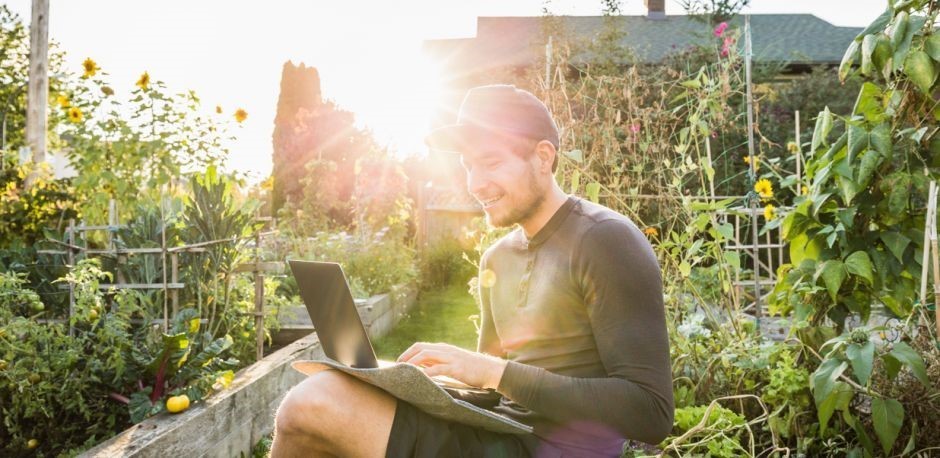 Man on a laptop in a garden surrounded by plants 