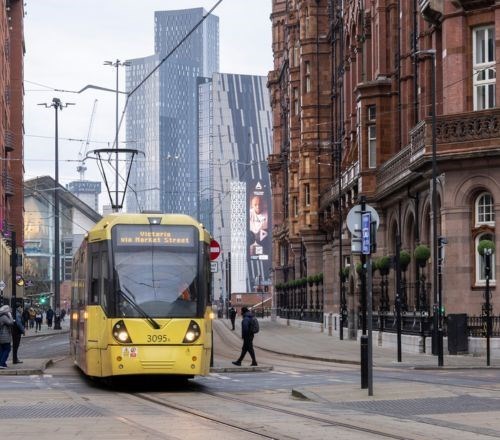 Yellow Metrolink tram driving through Manchester City Centre