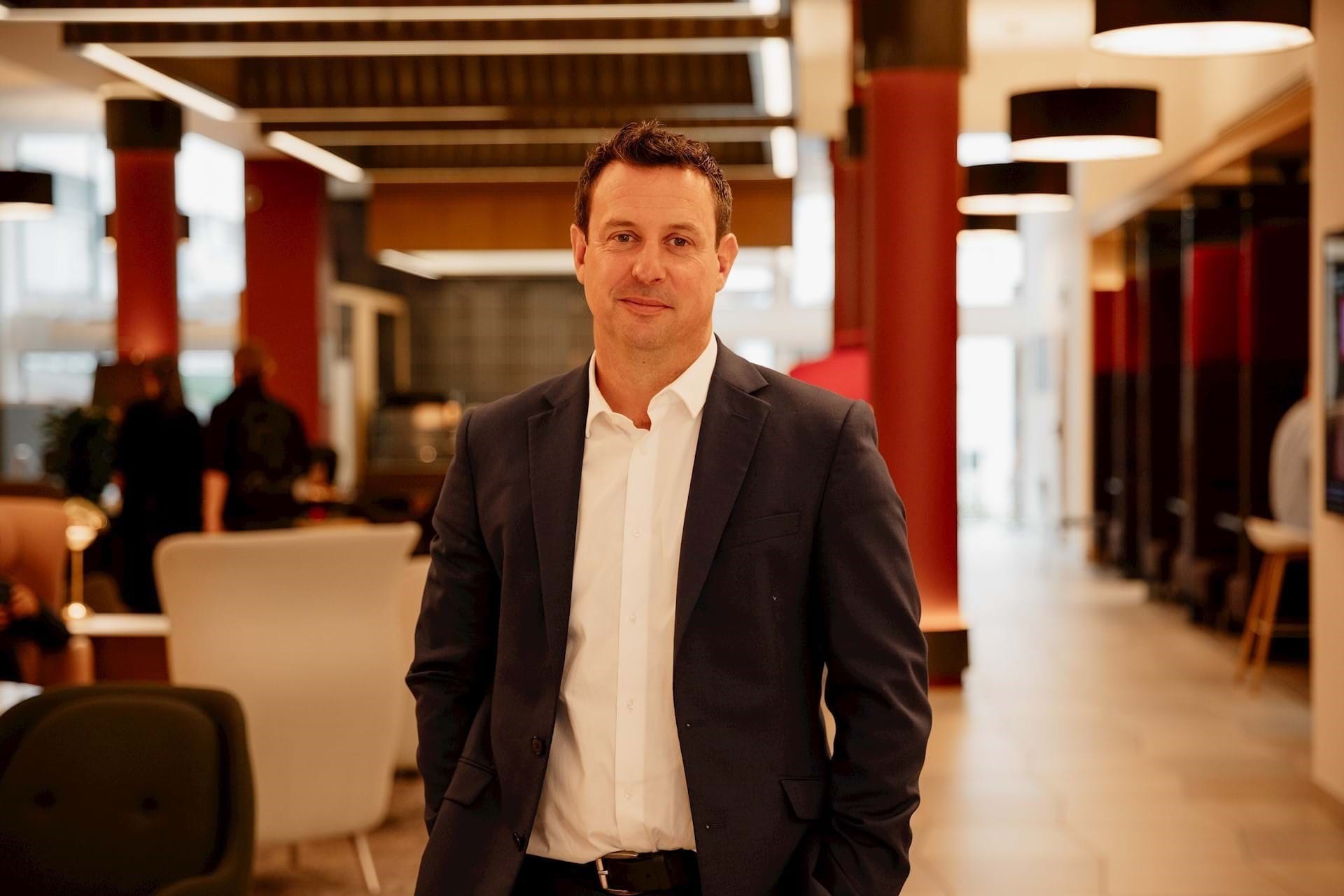 Jon-Paul Rimington wearing a white shirt with a dark suit jacket standing in a modern office