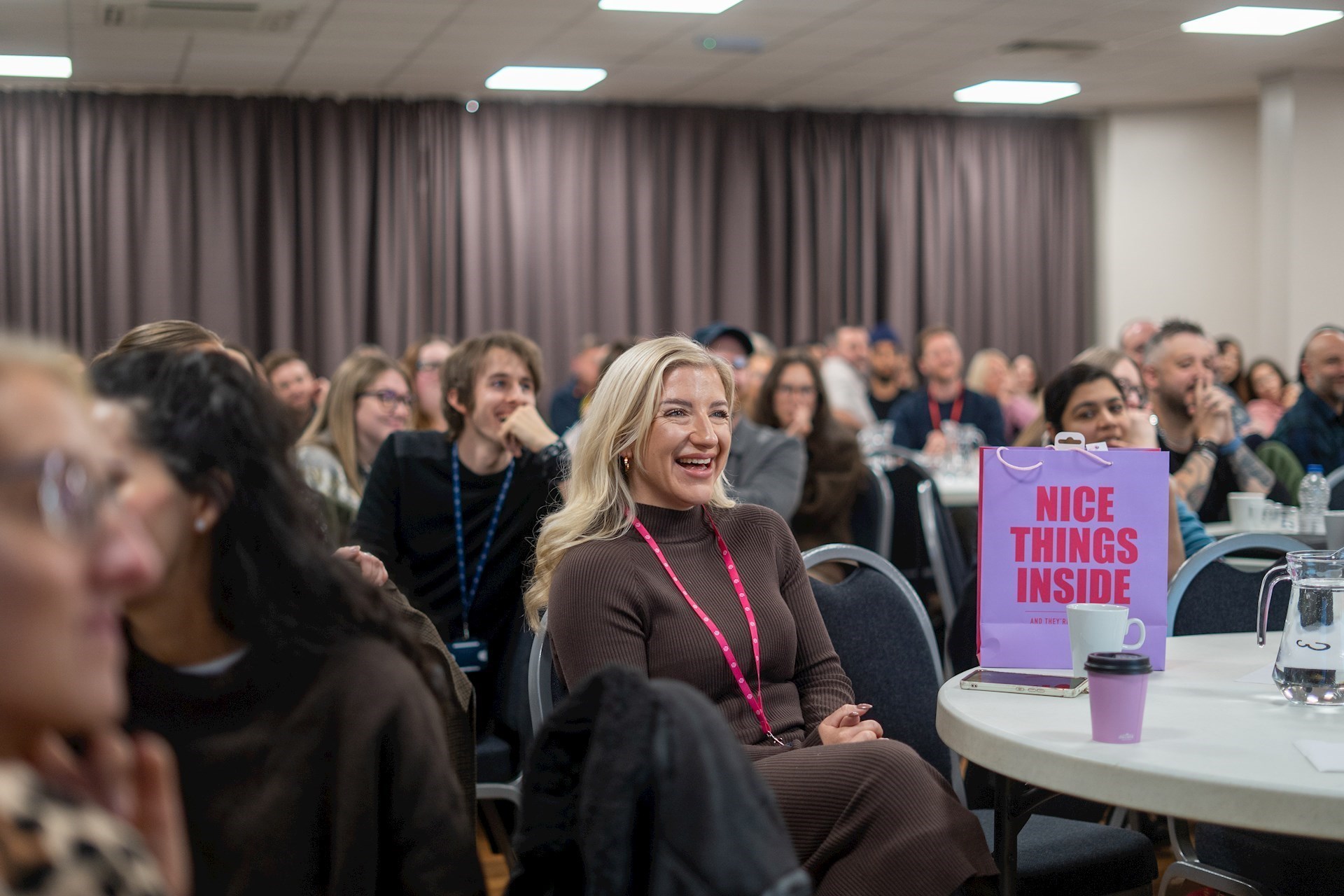 Colleague smiling with a room full of colleagues behind her in the background