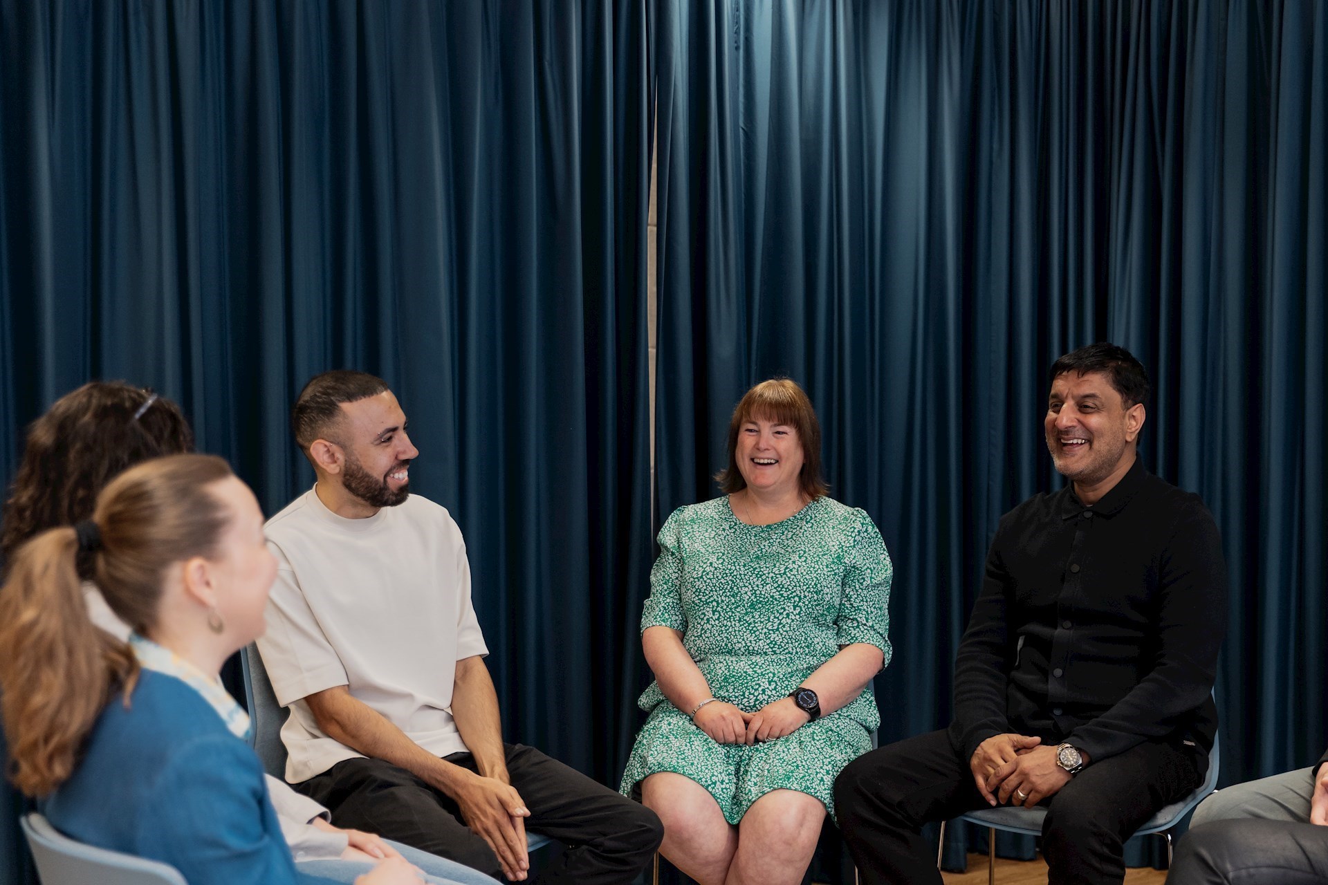 Five colleagues sitting in a circle smiling and laughing