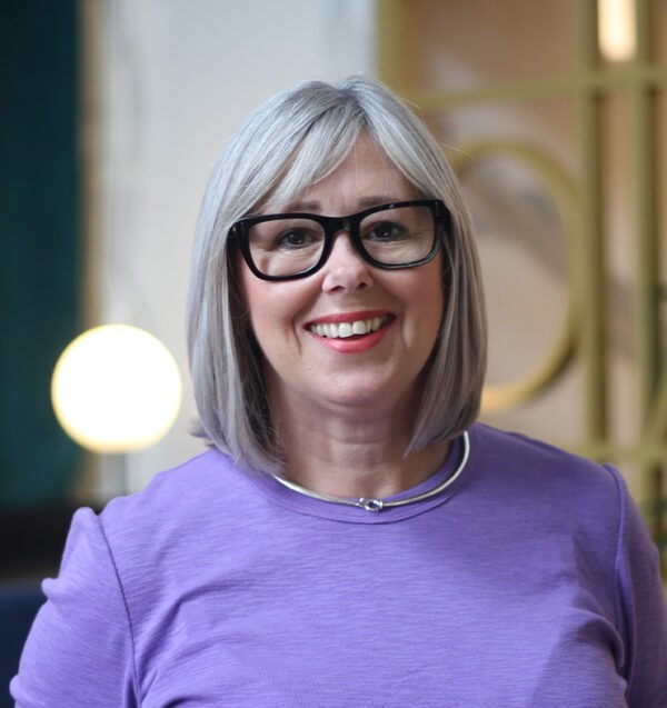 Lisa Riley wearing a purple top with a modern office in the background