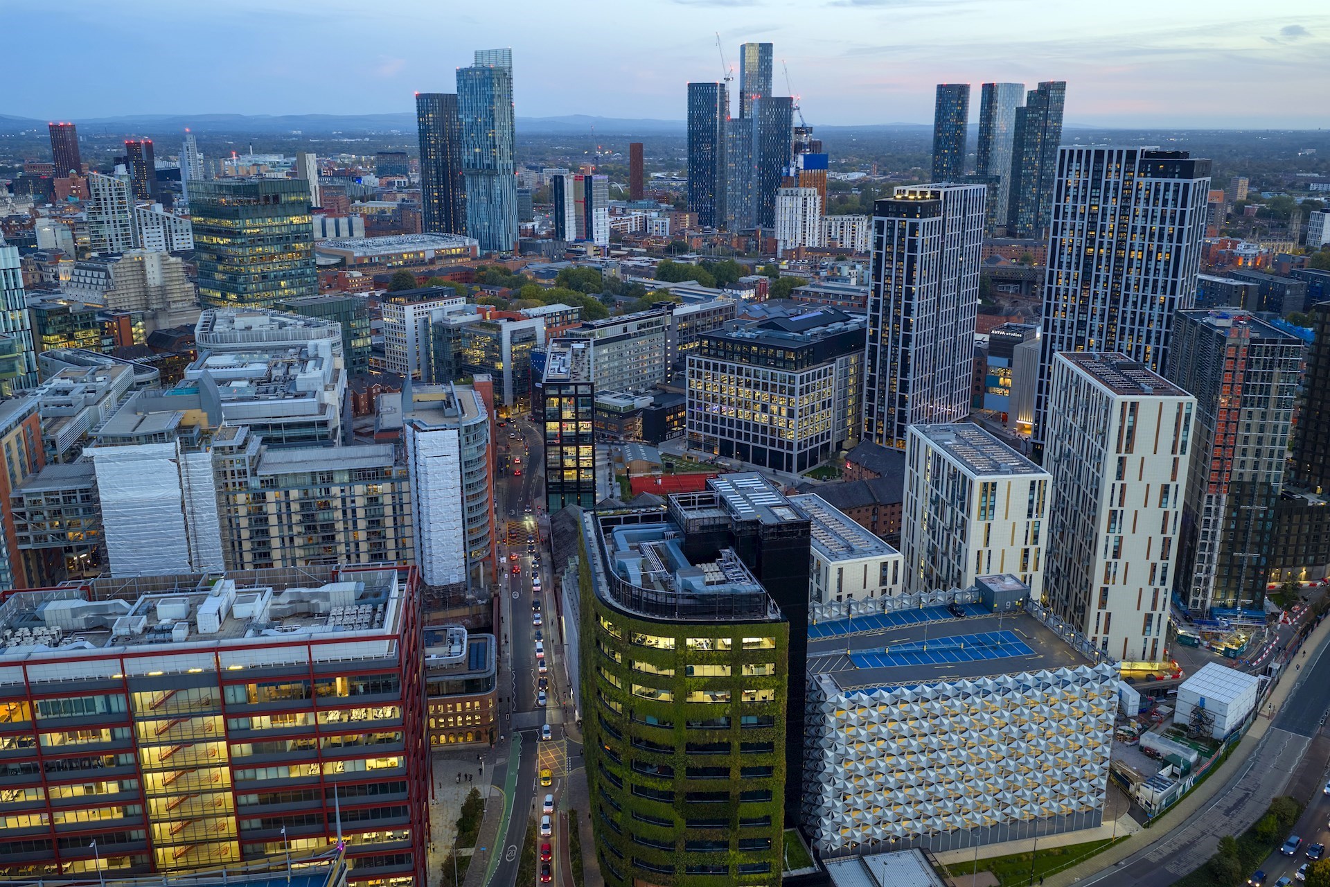 The Manchester skyline taken from above showing tall buildings with lights on in the evening