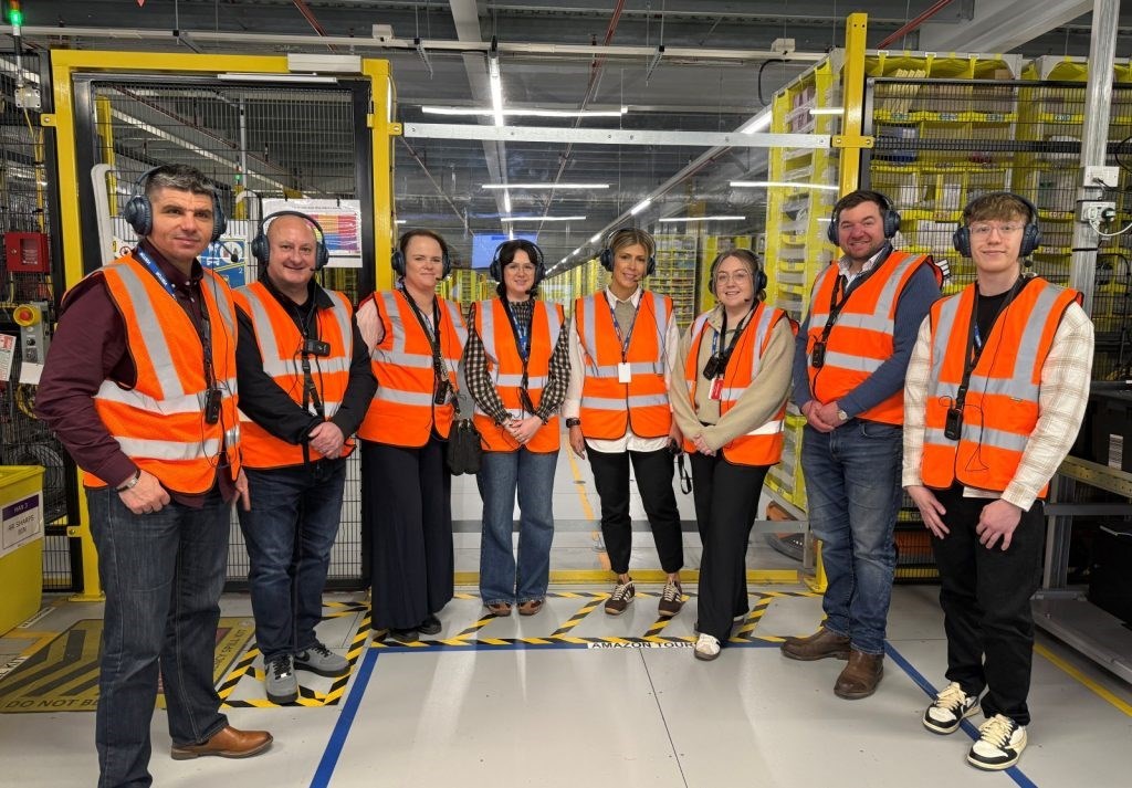 A group of people wearing high vis jackets and ear defenders standing in a factory setting 