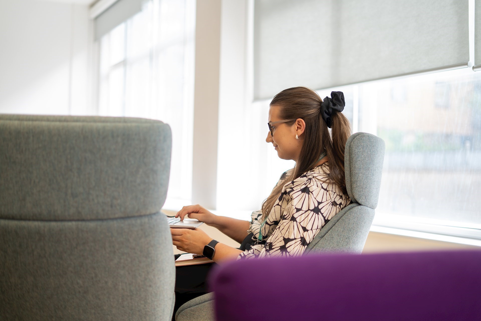Colleague sitting at a desk and working on her laptop with a window in the background