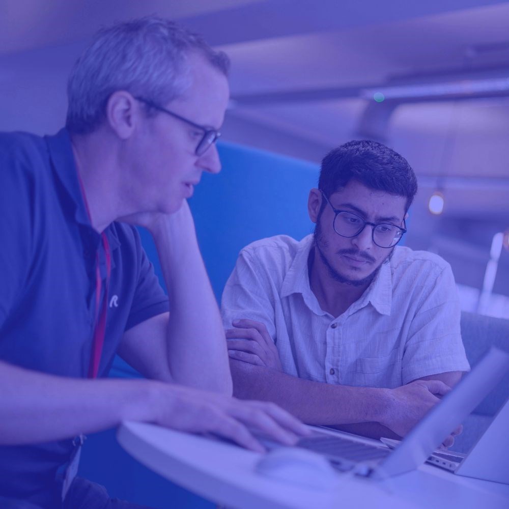 Two GC Insight colleagues looking at a laptop together with a dark purple tint